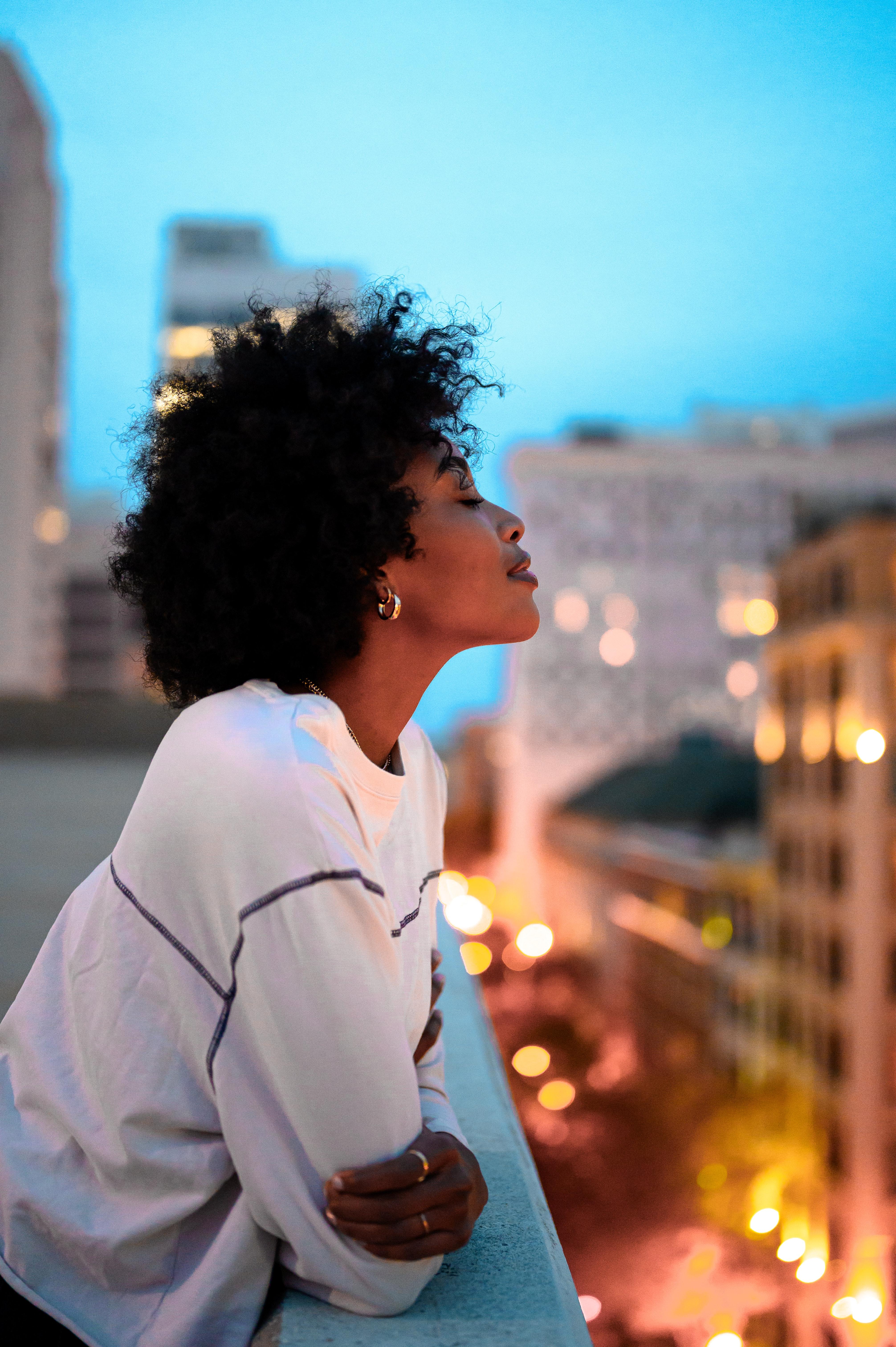 An African American woman stands on a city balcony at dusk