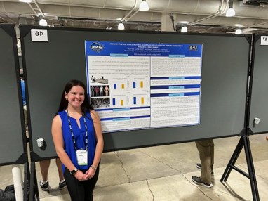 A UNE student poses in front of a research poster