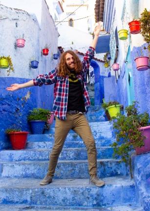 A student poses on an outdoor stairway amongst the blue-washed buildings of Chefchaouen, Morocco