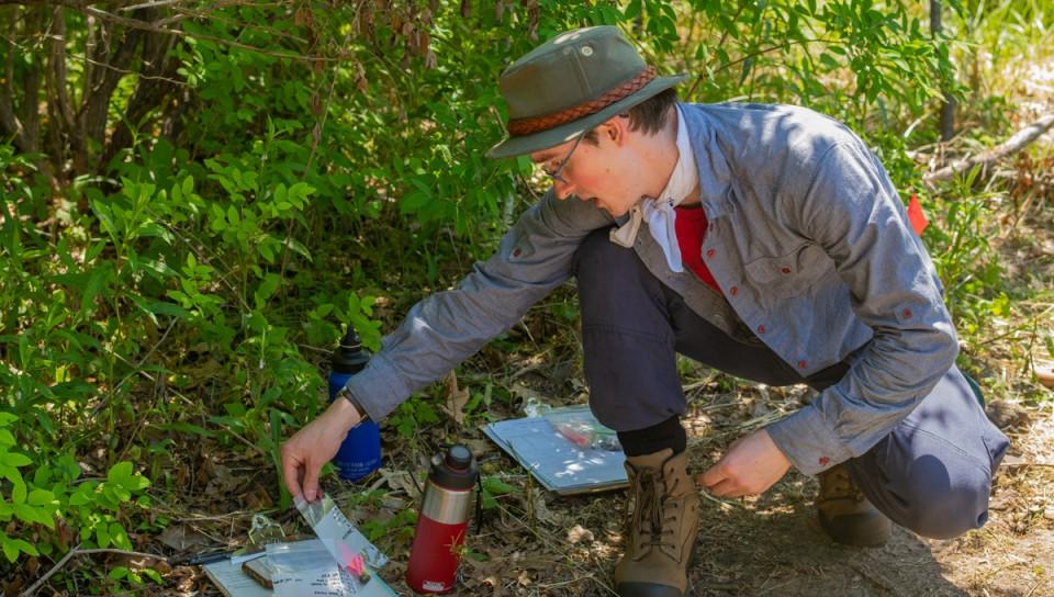 A U N E student picks up a plastic bag containing an artifact found at a dig site