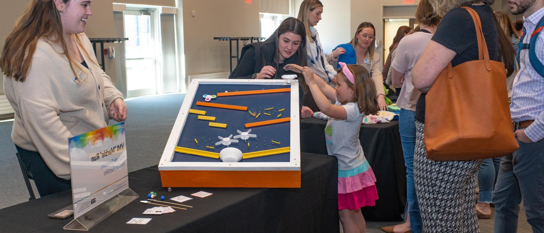 Students instruct a child how tp play with the marble run they built by hand