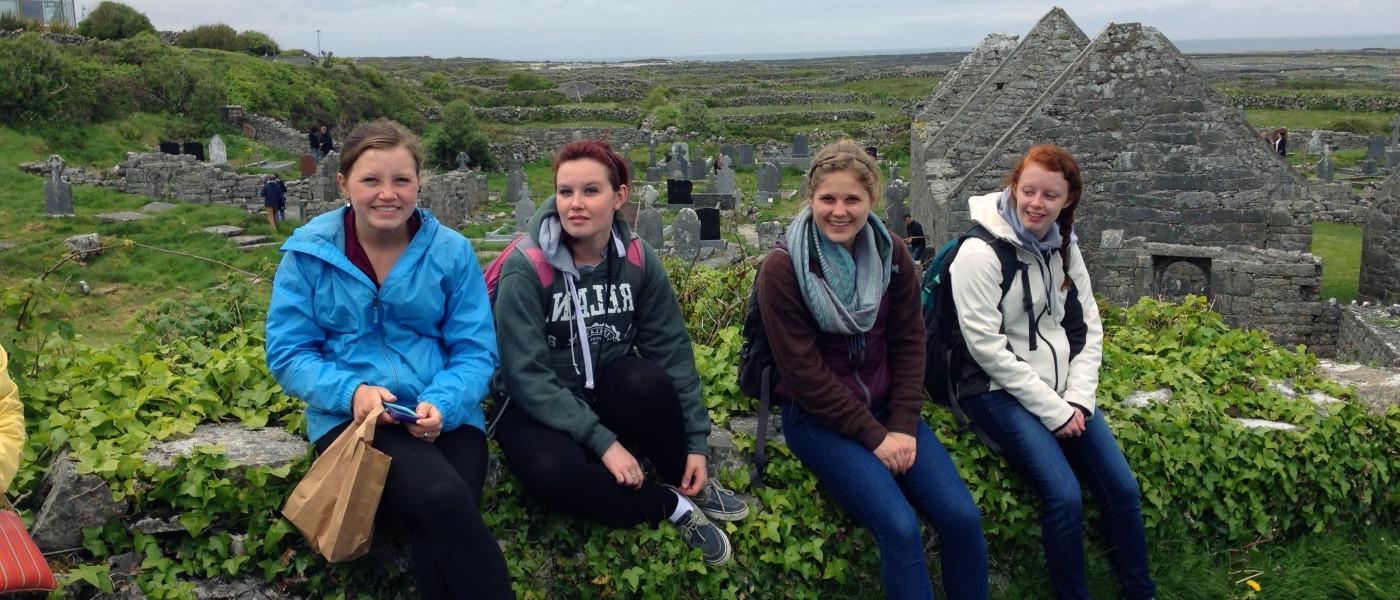 A group of U N E students sit on a stone wall at a rolling hillside cemetery in 爱尔兰