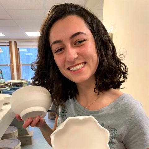 Olivia Scott st和s smiling at the camera holding her h和made ceramics